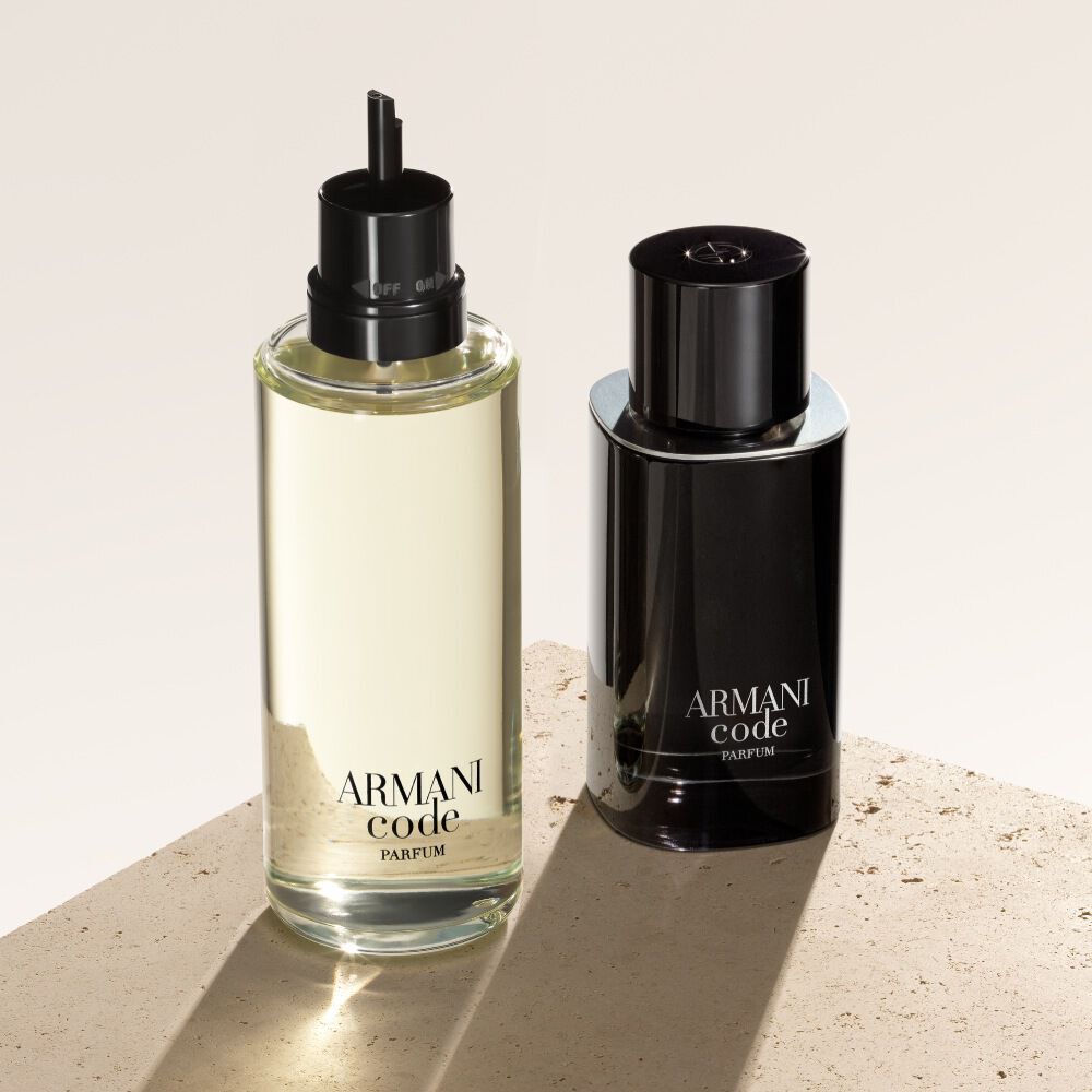 Dos frascos de Armani Code Parfum se muestran sobre un fondo texturizado de color beige. El frasco de la izquierda es una recarga, mostrando su apariencia mas ligera y transparente, mientras que el de la derecha muestra el clasico frasco negro opaco de la fragancia.