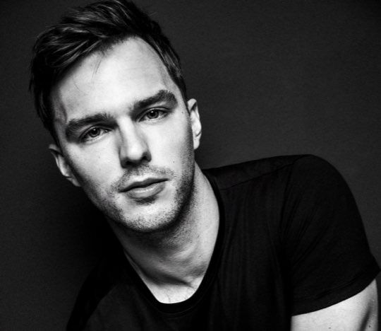 A portrait of a man with short hair wearing a black t-shirt, posed against a dark background. He has a serious expression and is leaning slightly forward.