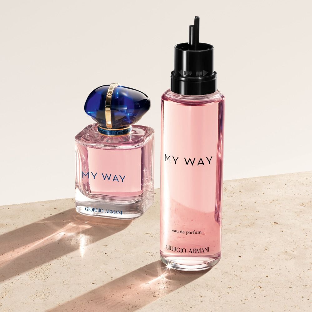 Un frasco y una recarga de Eau de Parfum My Way de Giorgio Armani. El frasco original, de un rosa suave con un tapon azul, se encuentra junto a su recarga rosa translucida, mas alta. Ambos descansan sobre una superficie palida y texturizada.