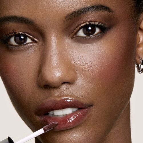 Close-up of a person applying lip gloss, showcasing smooth skin and defined features, with an emphasis on their glossy lips.