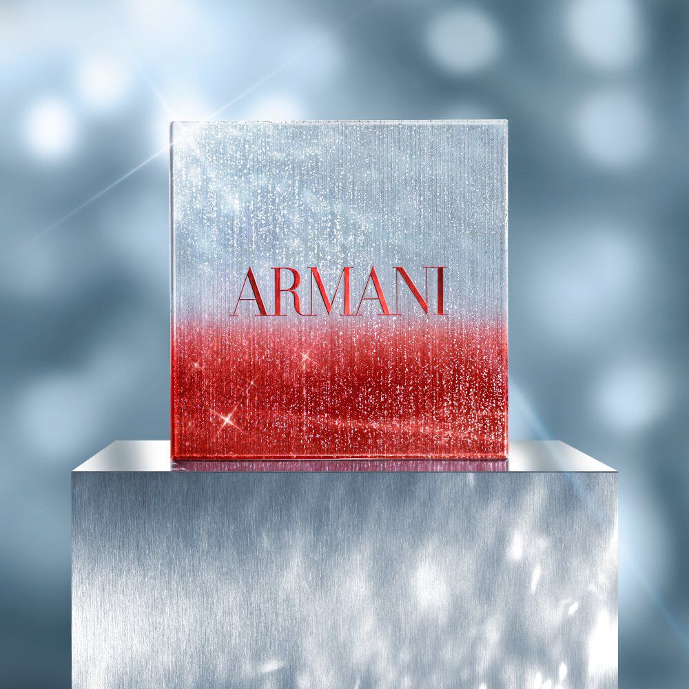 Square Armani holiday gift box in red and silver glitter gradient, displayed on a metallic pedestal with a sparkling, festive blue background.