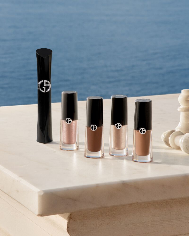Esenciales de ojos Armani: mascara y Eye Tints con piezas de ajedrez sobre marmol frente al mar. Simbolo de belleza estrategica y elegancia costera natural para un resplandor estival absoluto de puro lujo.