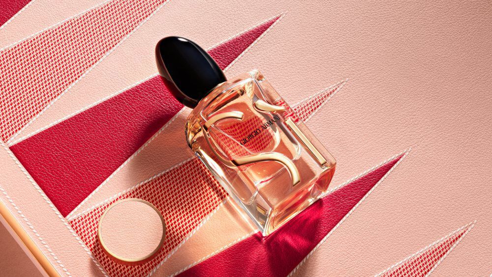 Armani Si Eau de Parfum bottle and cap from the Mother’s Day gift set on a pink and red geometric backgammon background.