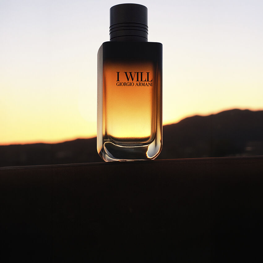 Frasco de la fragancia I WILL de Giorgio Armani sobre un paisaje al atardecer.