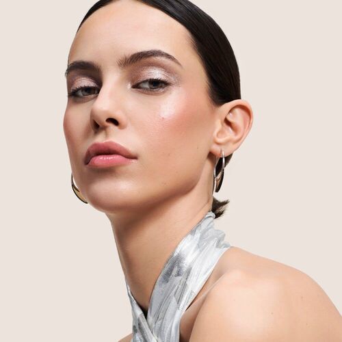 Mujer con maquillaje sutil y peinado elegante, luciendo un collar plateado sobre fondo neutro.