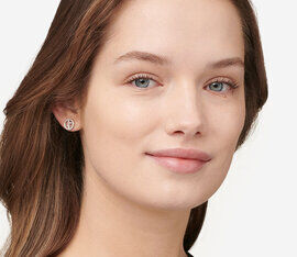 A close-up of a young woman with long, straight hair, wearing small stud earrings and a subtle smile. She has a natural makeup look and is facing the camera.
