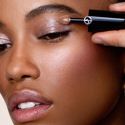 A close-up of a person applying shimmering eyeshadow with a brush applicator, showcasing radiant skin and a focus on eye makeup.
