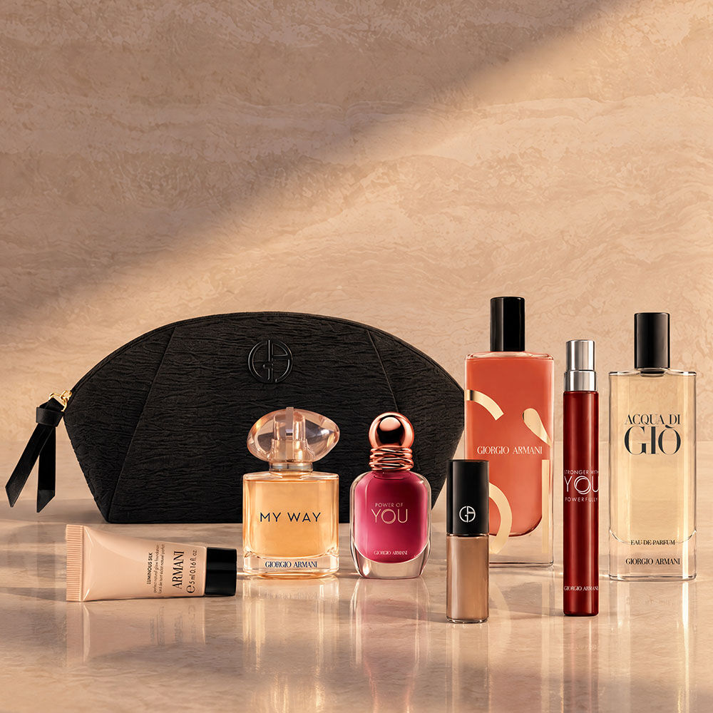 Un neceser negro de Armani Beauty junto a fragancias, maquillaje y productos de cuidado de la piel sobre un fondo beige.