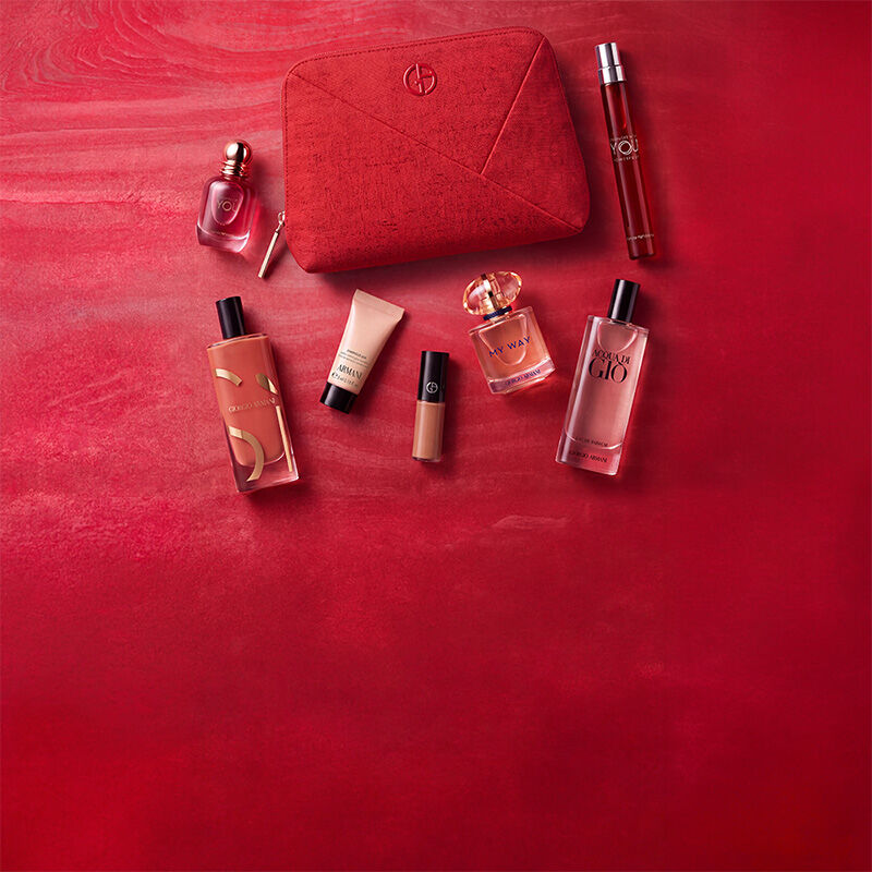 Tres productos Armani Beauty — un producto de labios, la fragancia Power of You y la base de maquillaje Luminous Silk — sobre un fondo rojo texturizado.