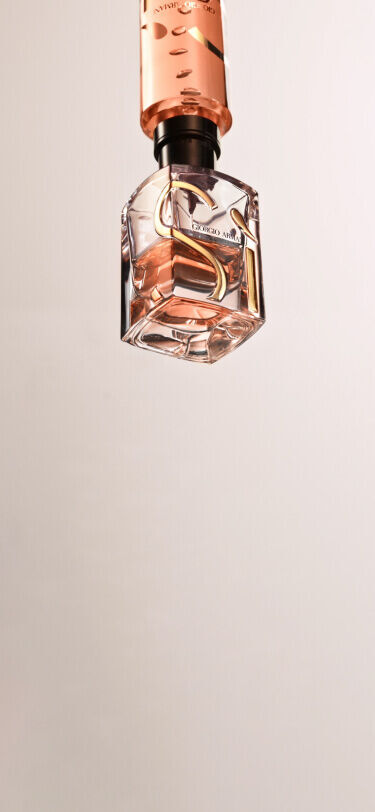 Botella de perfume elegante en tonos rosados, suspendida sobre un fondo claro.