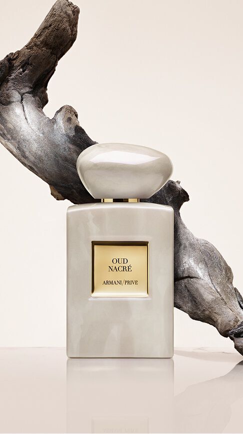 Armani/Prive Oud Nacre: un frasco con reflejos nacarados frente a una pieza de madera a la deriva esculpida, capturando la nobleza eterna del Oud en una estela de absoluta pureza y elegancia.