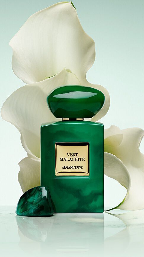 Armani/Prive Vert Malachite: un vibrante frasco verde esmeralda con tapon de piedra, frente a lirios blancos inmaculados, capturando la frescura radiante de un jardin ruso banado por una belleza luminosa y serena.