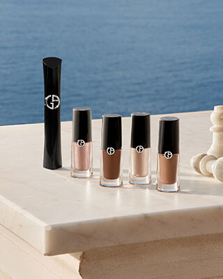 Esenciales de ojos Armani: mascara y Eye Tints con piezas de ajedrez sobre marmol frente al mar. Simbolo de belleza estrategica y elegancia costera natural para un resplandor estival absoluto de puro lujo.