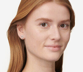 A close-up of a woman with long, straight hair wearing simple stud earrings, smiling gently at the camera.