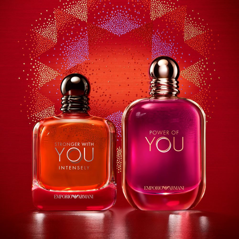 Dos fragancias de Emporio Armani, Stronger With You Intensely y Power of You, sobre un fondo festivo rojo.​
