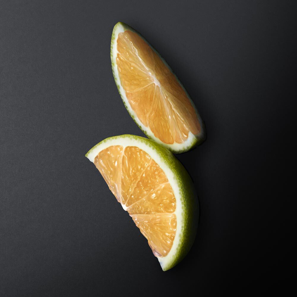 Two wedges of orange citrus fruit on a dark background. The wedges are bright orange with a green rind, showcasing their juicy interior.
