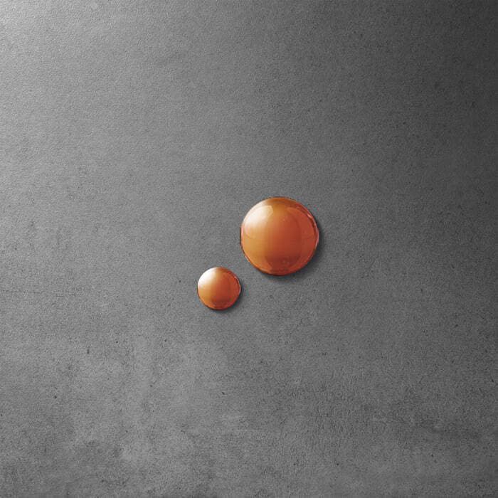 Two small, reflective water droplets sit on a textured gray surface.