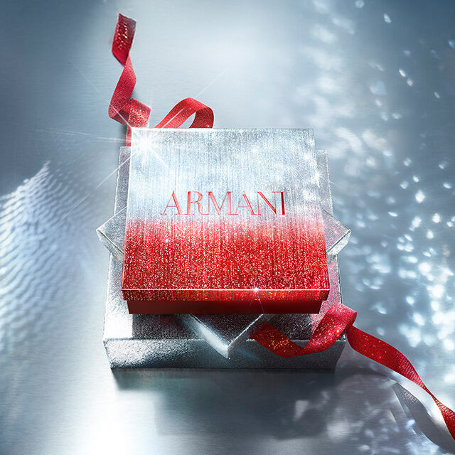 Caja de regalo Armani brillante con cinta roja sobre superficie reluciente.