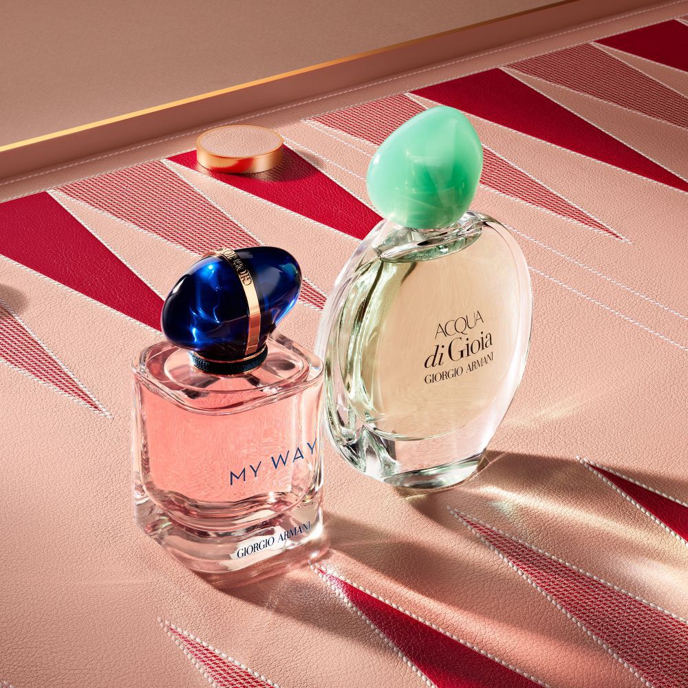 Armani My Way Eau de Parfum bottle and Acqua di gioia Eau de parfum bottles on a pink and red geometric backgammon board background.