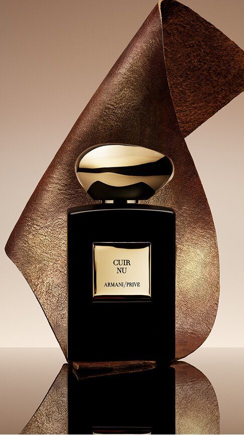Armani/Prive Cuir Nu: un elegante frasco negro con tapon dorado, envuelto en una cinta de cuero texturizado, encarnando la sensualidad de la piel desnuda y el refinamiento supremo de una estela amaderada.