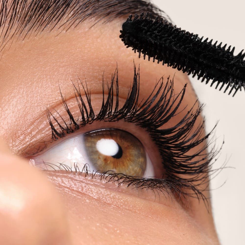 Cercania de un ojo con pestanas largas mientras se aplica mascara de pestanas negra.