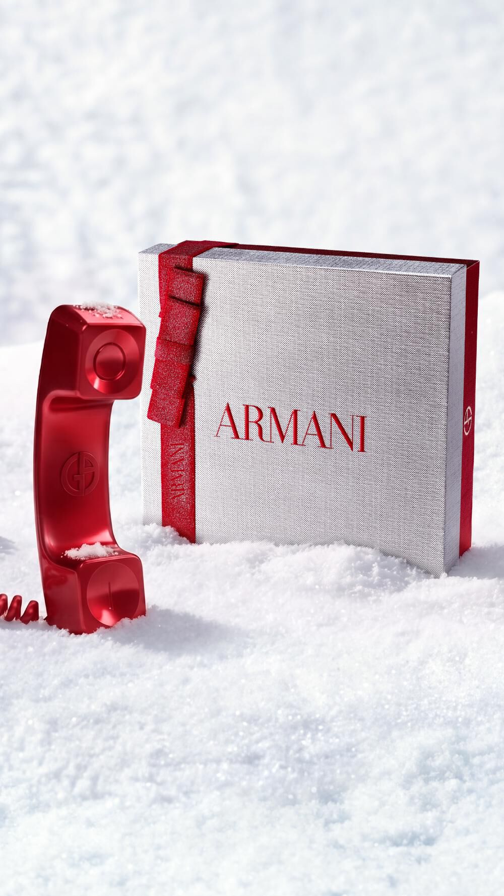 Caja de regalo de Navidad Armani Beauty junto a un telefono rojo que representa la atencion al cliente, en un entorno nevado.