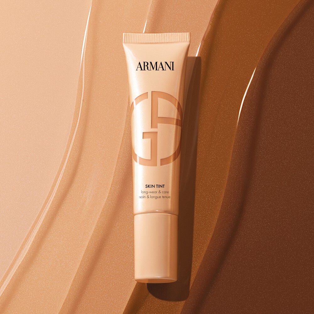 Tubo de Armani Skin Tint sobre muestras de base liquida de varios tonos.