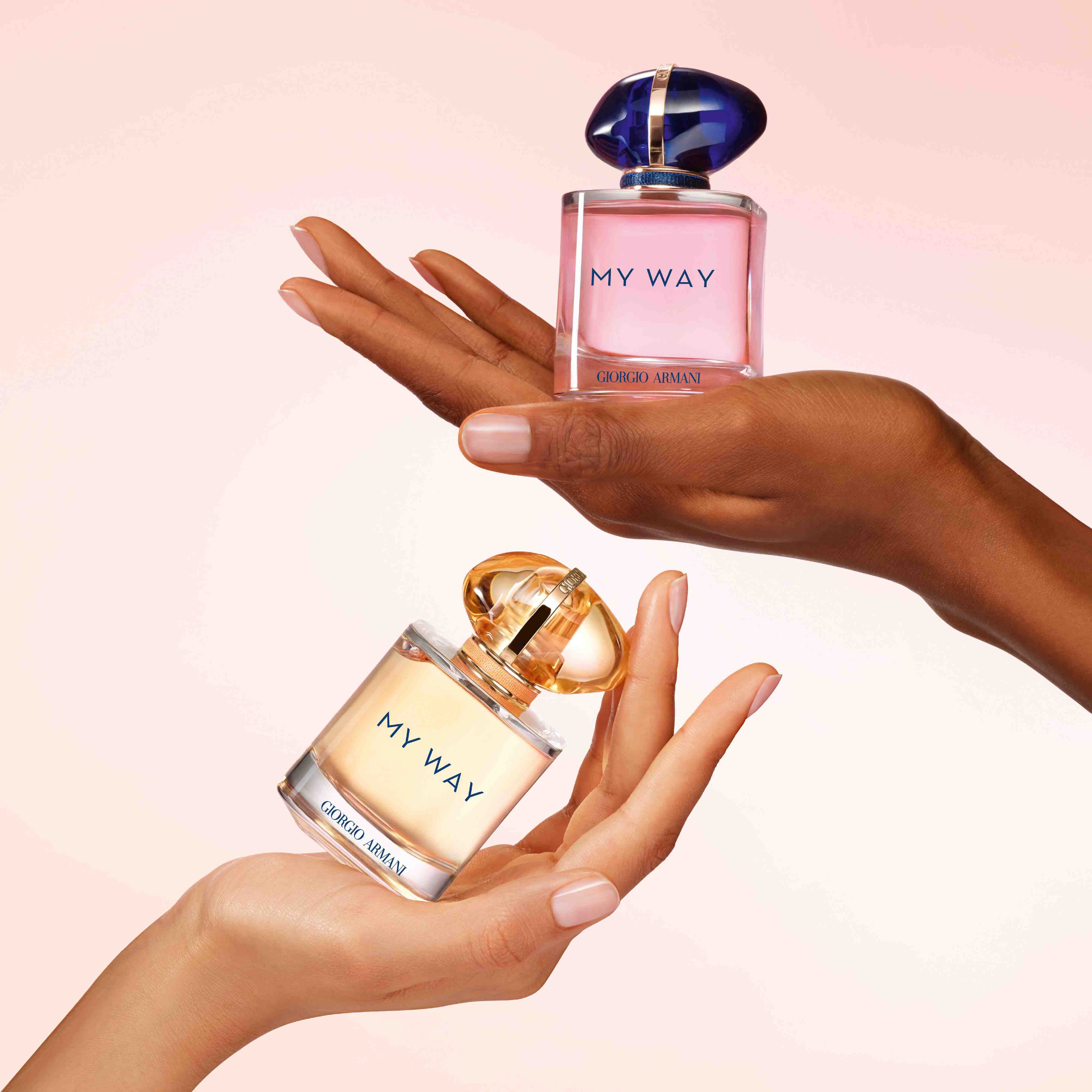 Dos manos de diferentes tonos de piel sosteniendo cada una un frasco de la fragancia My Way de Giorgio Armani.