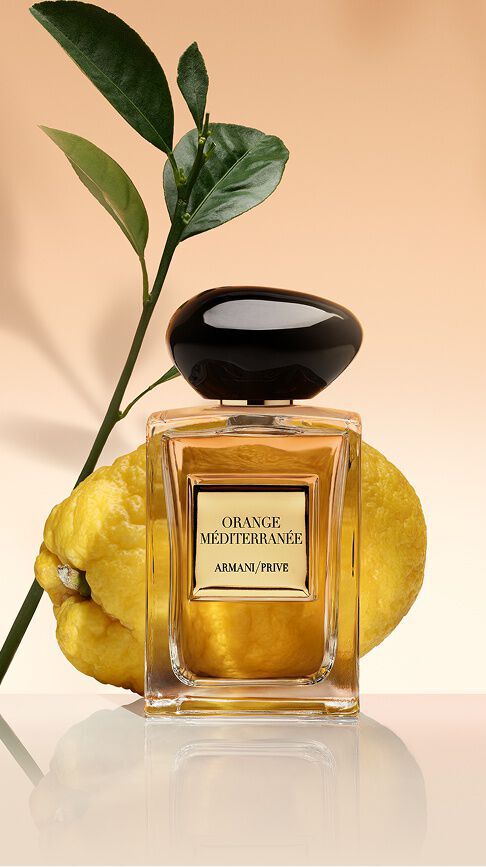 Armani/Prive Orange Mediterranee: un frasco de nectar dorado, frente a un citrico fresco y hojas verdes, que irradia el calor banado por el sol del Mediterraneo.
