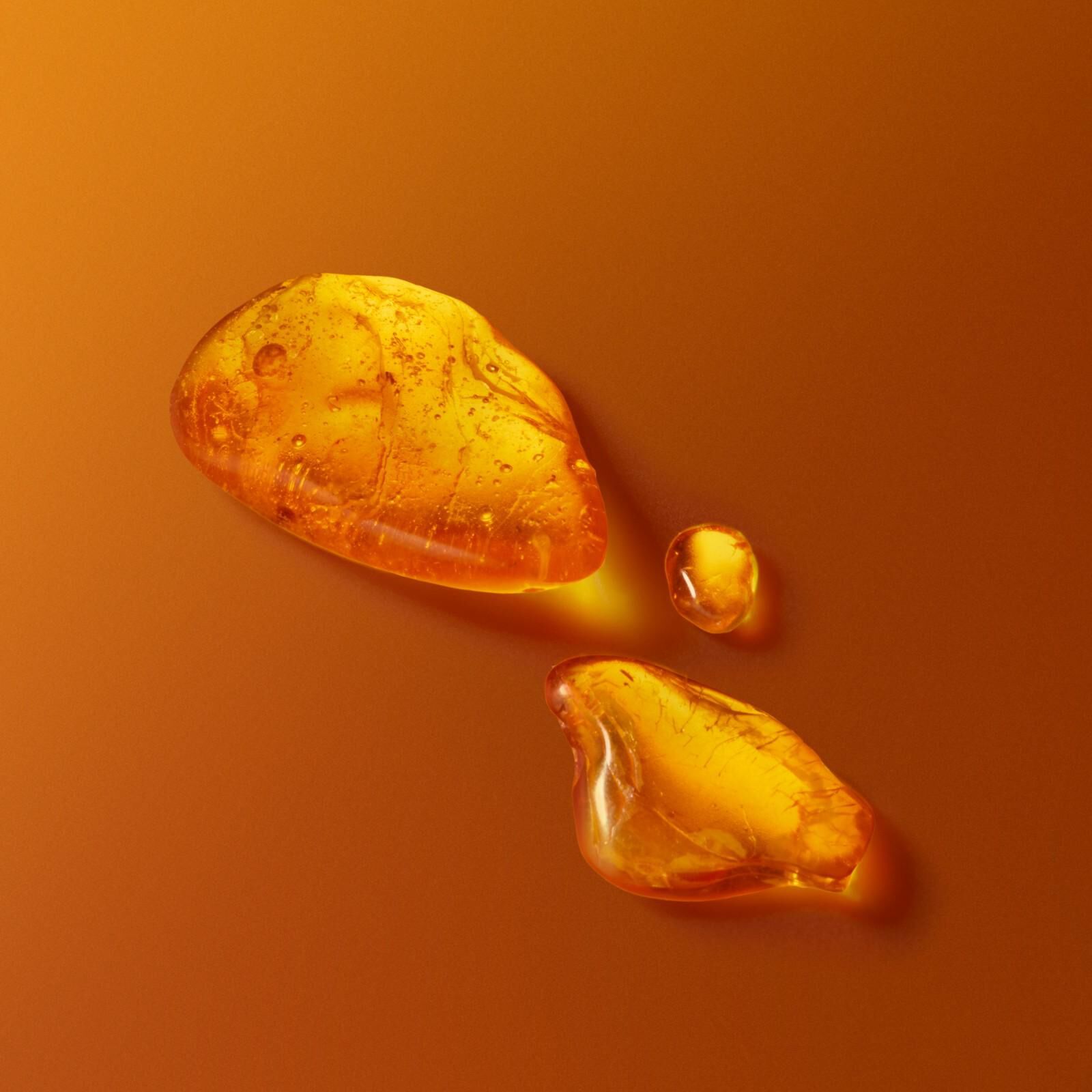 Gotas de ambar dorado y trozos de resina sobre un fondo naranja calido, representando la esencia de la fragancia.