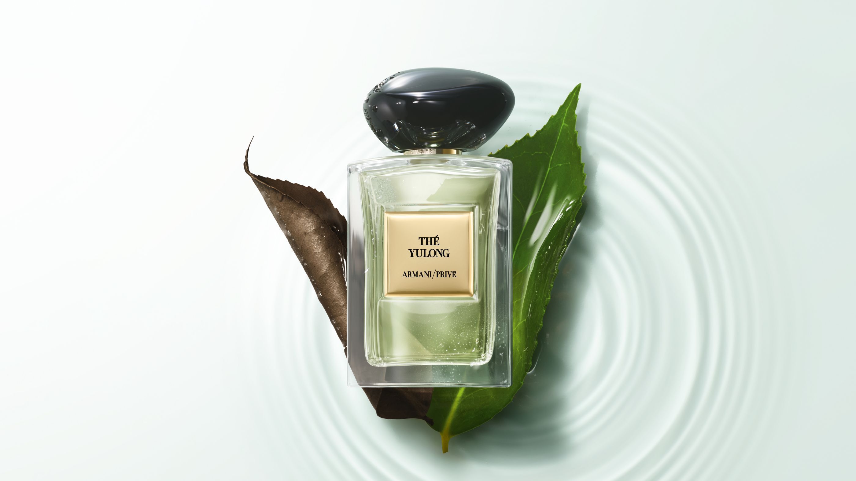 Frasco de perfume Armani/Prive "The Yulong" sobre hojas en agua con ondas.