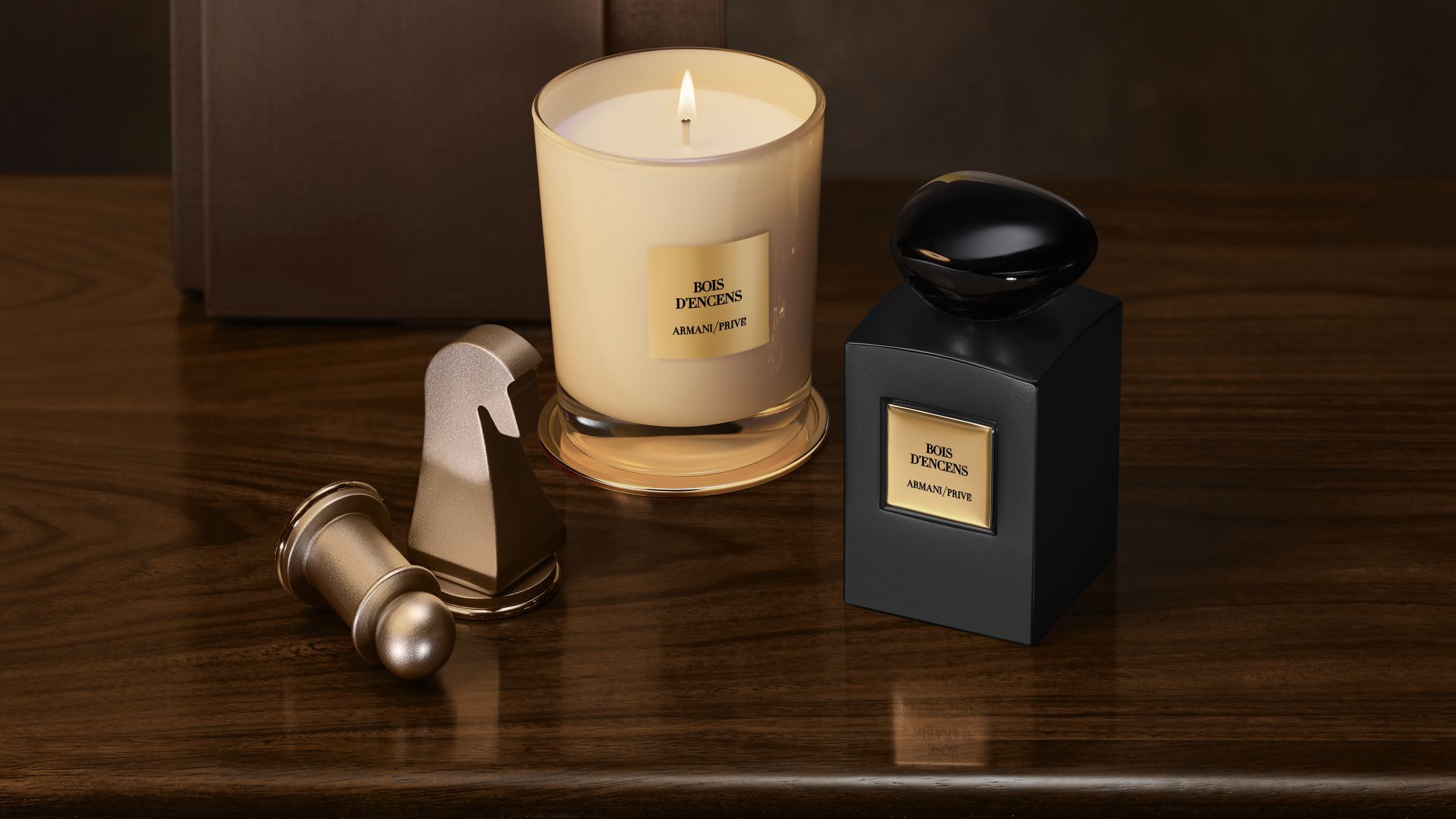 Frasco de perfume y vela encendida Armani/Prive Bois d'Encens junto a piezas de ajedrez sobre una mesa de madera.