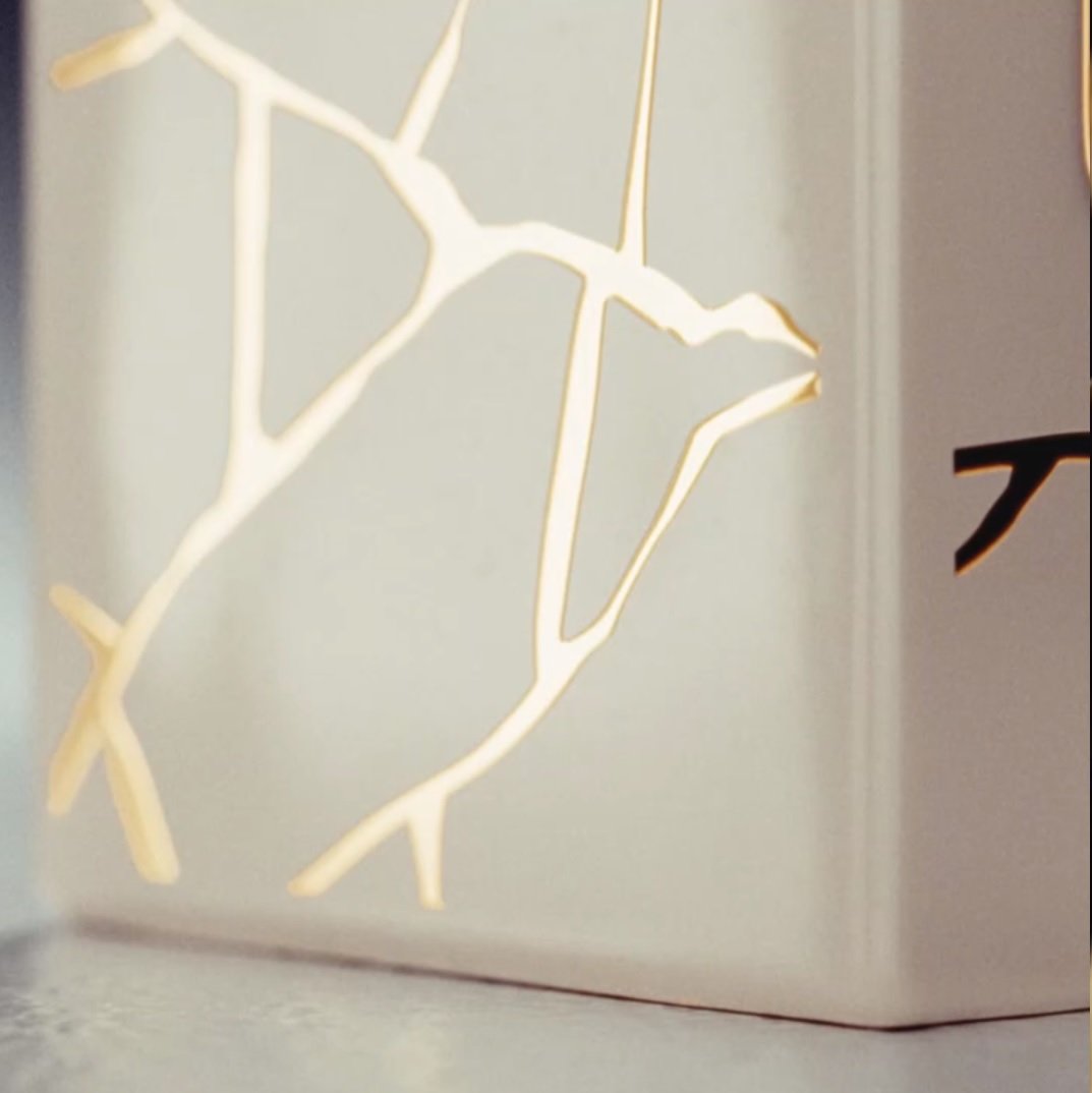 Detalles de una lámpara decorativa blanca con un diseño de líneas doradas que simulan ramas.