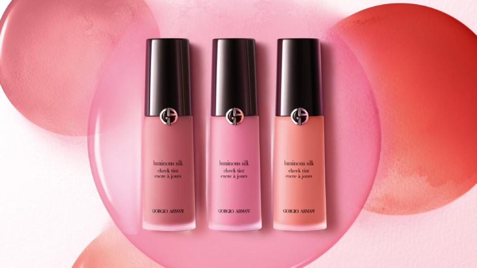 Tres frascos de rubor líquido Luminous Silk de Giorgio Armani en tonos rosa, sobre un fondo de suaves manchas de color.