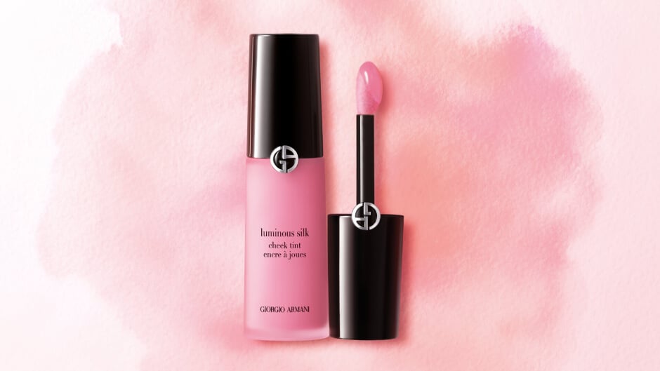A bottle of Giorgio Armani Luminous Silk Cheek Tint in soft pink, with a wand applicator, against a pastel pink backdrop.